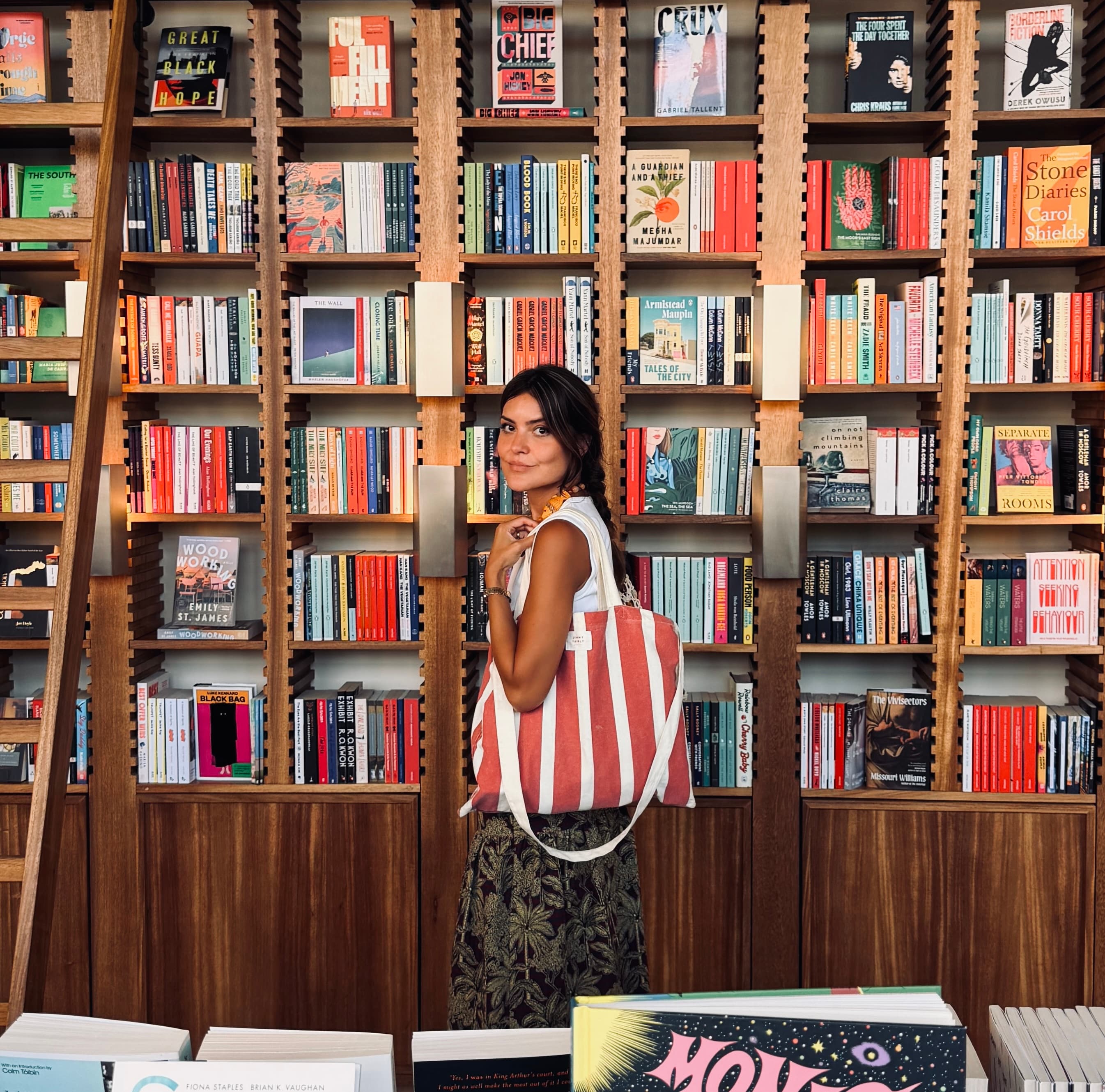 The Riposte curator standing in front of colourful bookshop shelves.